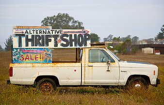Rusty white pickup truck with hand-painted thrift shop sign in field