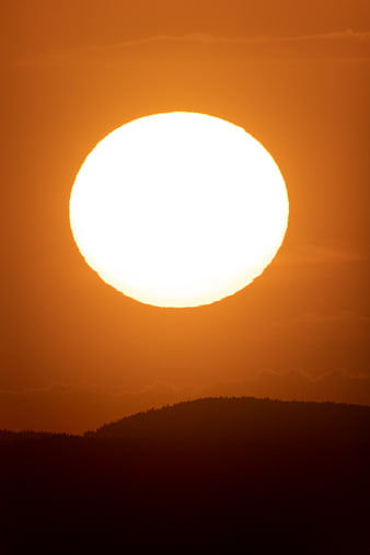 Giant Orange Sun Setting Over Silhouetted Mountain Ridge