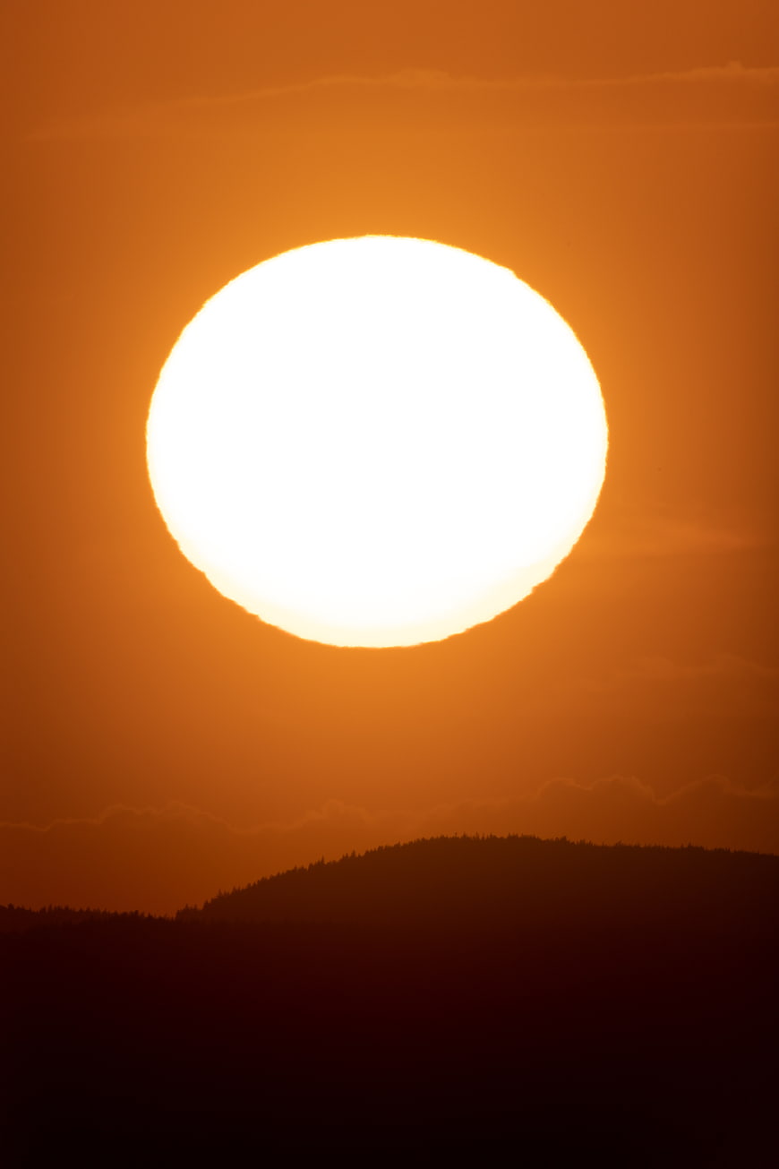 Giant Orange Sun Setting Over Silhouetted Mountain Ridge