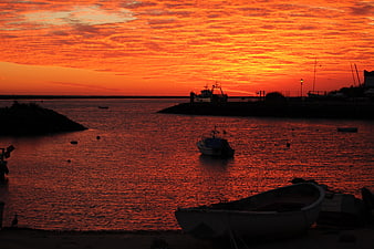 Dramatic orange sunset over harbor with silhouetted boats
