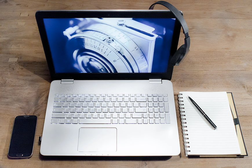 Top view of laptop, smartphone, notebook, and headphones on wooden desk