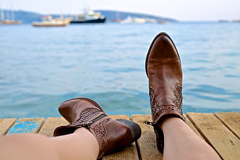 Woman's brown leather boots resting on wooden dock by sea