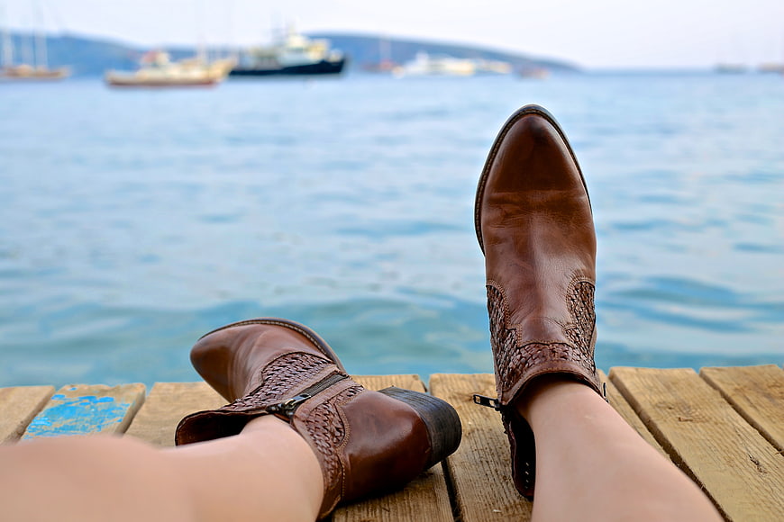 Woman's brown leather boots resting on wooden dock by sea