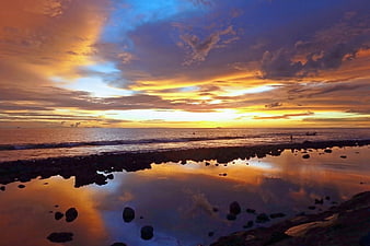 Vibrant sunset over ocean with rocky tide pool reflection