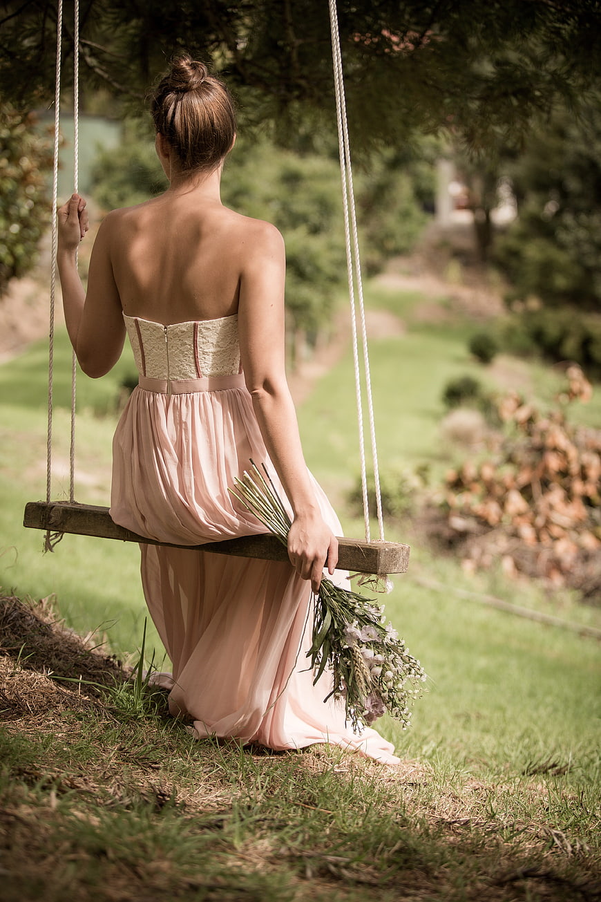 Woman in Pink Dress Sitting on Wooden Swing with Bouquet