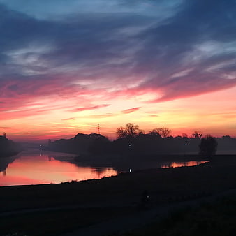 Vibrant pink and orange sunrise over a misty river landscape