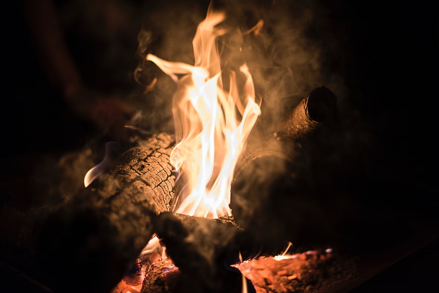 Close-up of burning logs and flames in a dark campfire