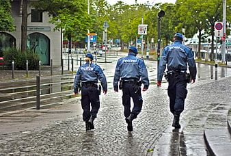 Three German Police Officers Walking On Wet Cobblestone Street