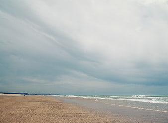 Wide sandy beach under dramatic cloudy sky with ocean waves