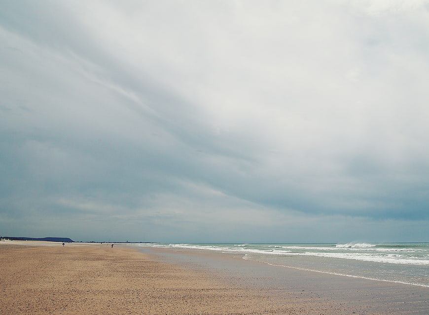 Wide sandy beach under dramatic cloudy sky with ocean waves