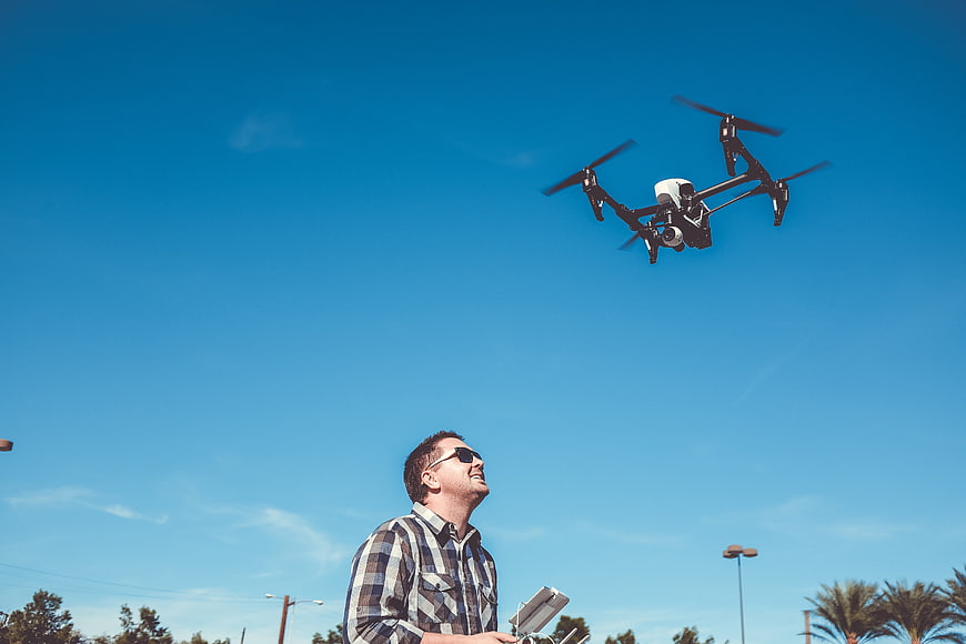 Man flying drone outdoors against blue sky