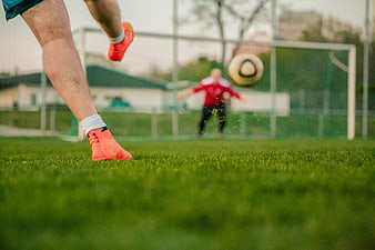 Low angle soccer player kicking ball on green pitch