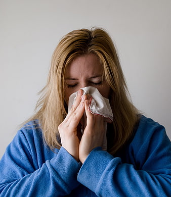 Woman in blue robe blowing nose with tissue
