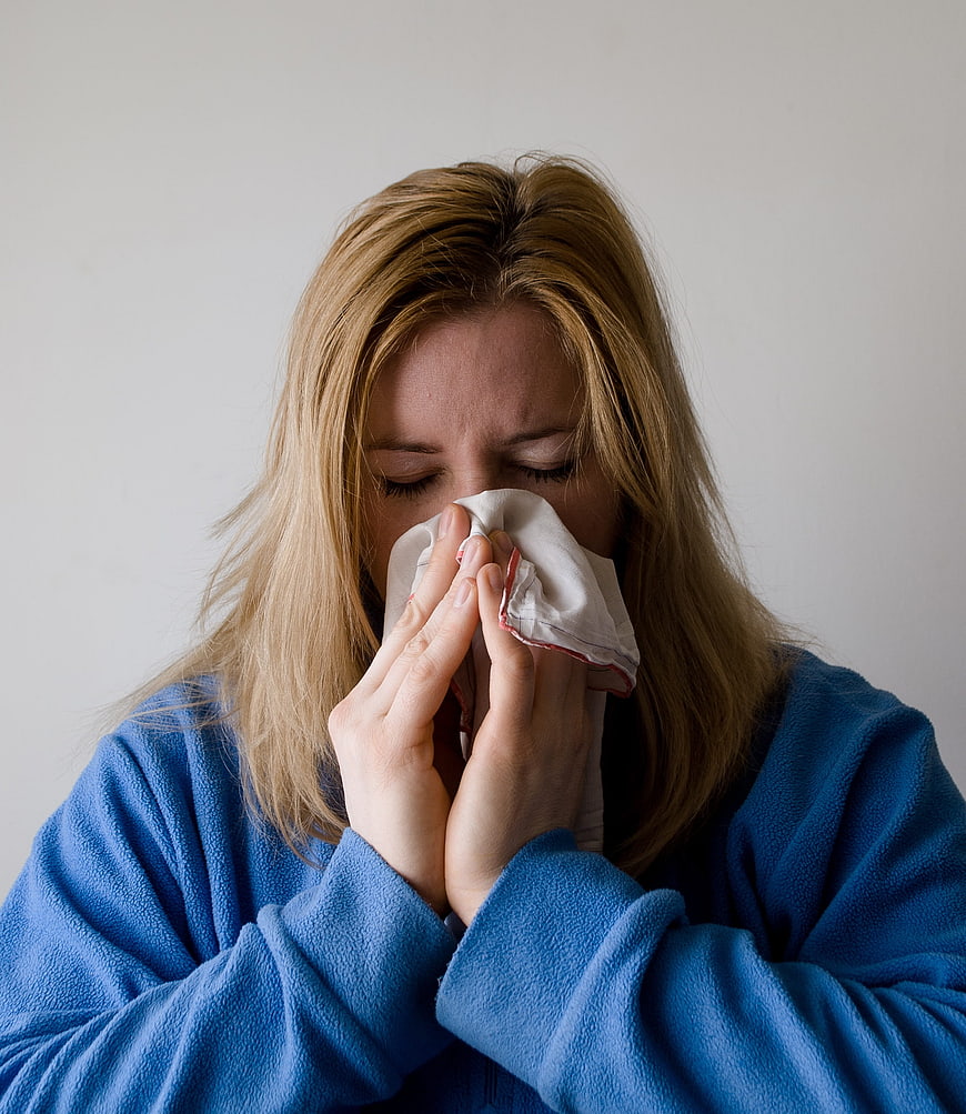Woman in blue robe blowing nose with tissue