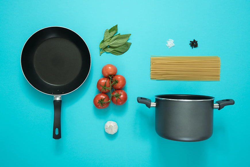Flat lay of pasta ingredients and cookware on blue background