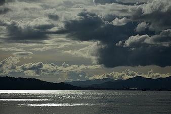 Dramatic Cloudy Sky Over Sparkling Sea and Silhouette Mountains