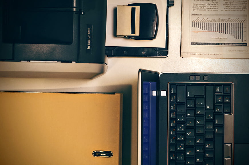 Top-down view of office desk with laptop, printer, and folder
