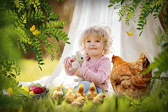 Cute little girl with Easter eggs, chicks, and a hen in a garden