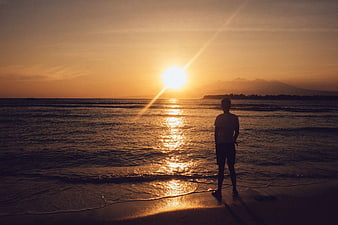 Silhouette of Man Watching Golden Sunset Over Ocean