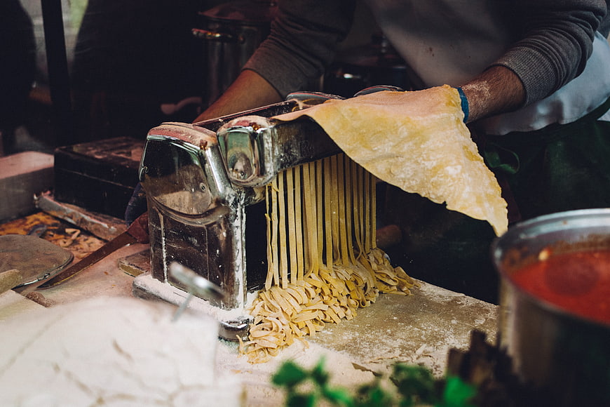 Homemade pasta being cut with a manual machine