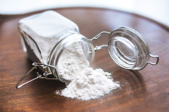 Spilled white flour from glass jar on wooden table