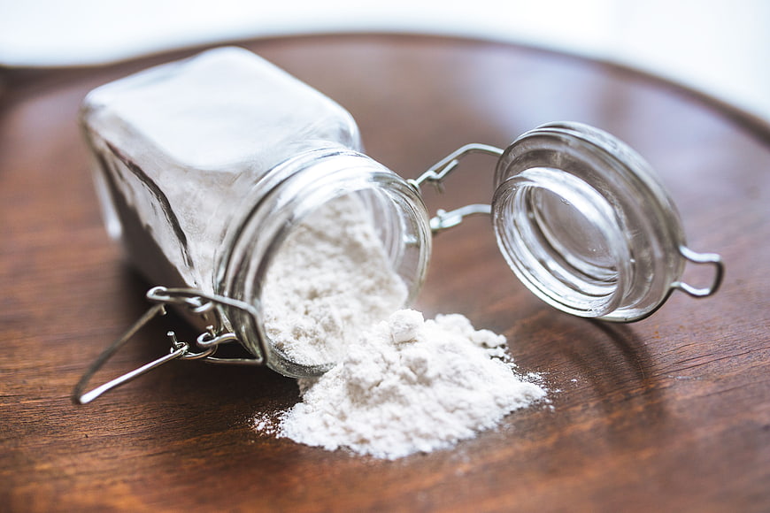 Spilled white flour from glass jar on wooden table
