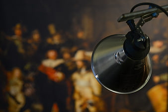 Modern metal lamp illuminating blurred Rembrandt Night Watch painting