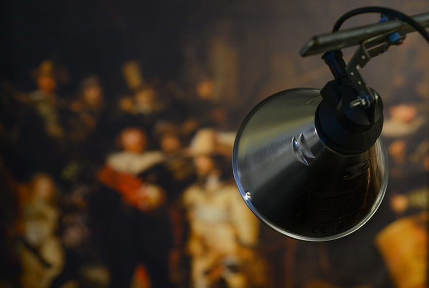 Modern metal lamp illuminating blurred Rembrandt Night Watch painting