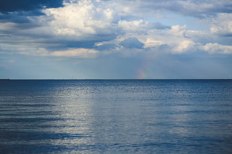 Serene ocean horizon with faint rainbow and dramatic clouds