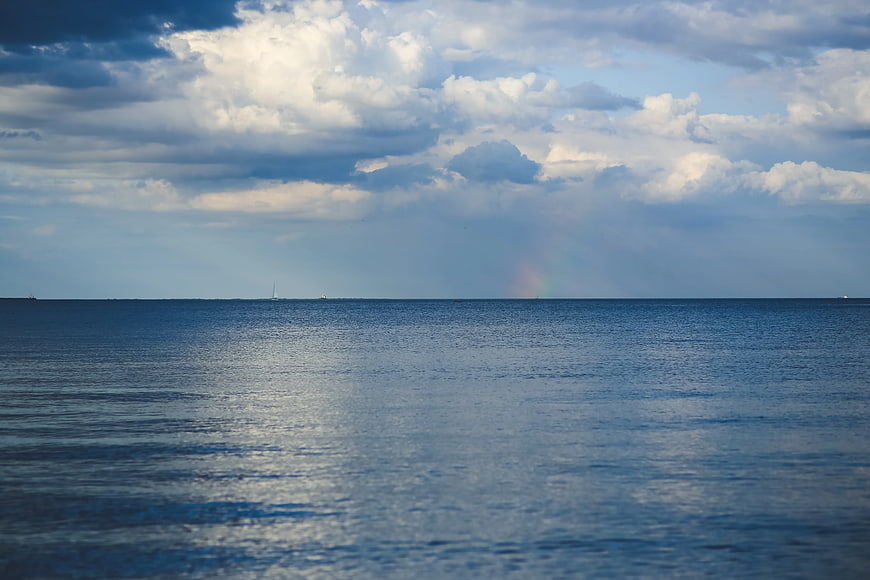 Serene ocean horizon with faint rainbow and dramatic clouds