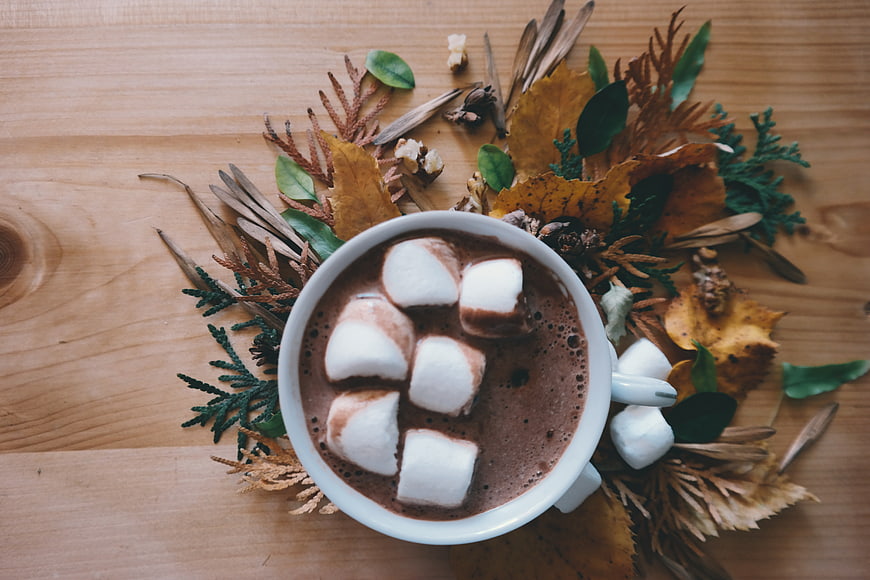 Overhead view of hot chocolate with marshmallows and autumn leaves