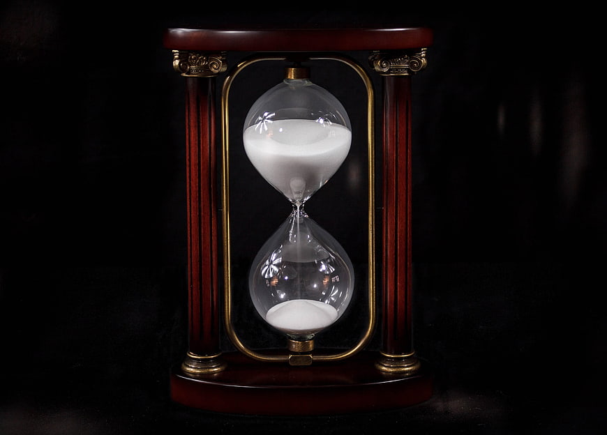 Vintage wooden hourglass with white sand on black background