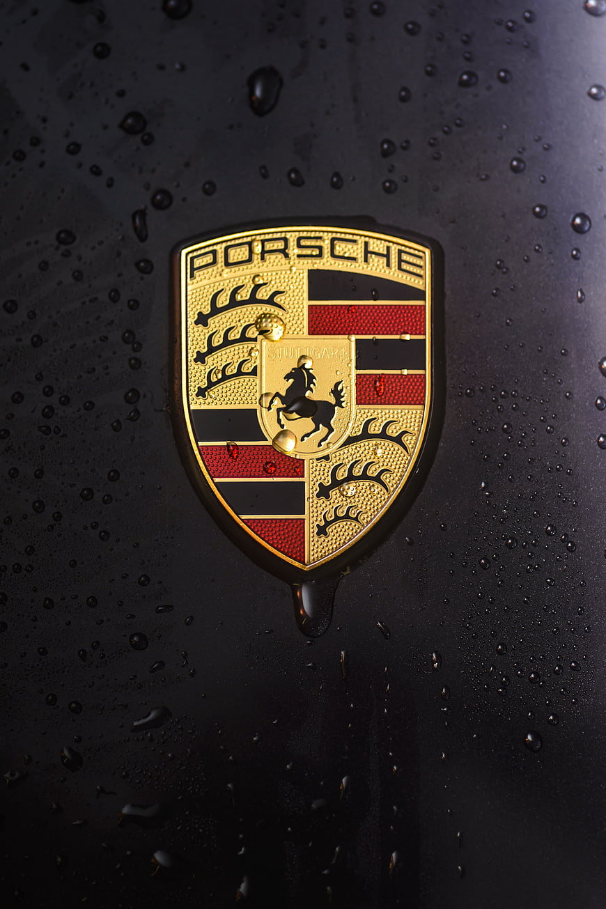 Porsche Emblem Close-Up With Water Droplets On Black Car Surface