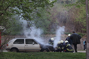 Firefighters extinguishing smoke from a burning white car outdoors
