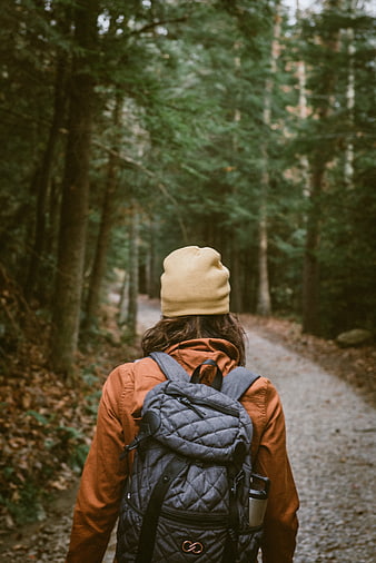 Woman hiking on forest path with backpack and beanie