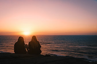 Silhouette of Two Friends Watching Sunset Over Ocean