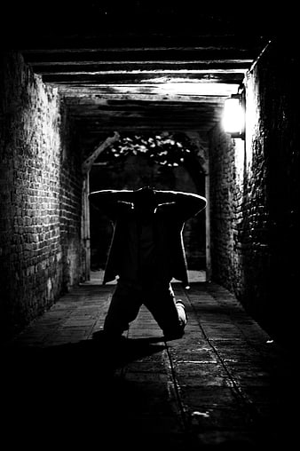 Dramatic Silhouette of Man Kneeling in Dark Brick Corridor