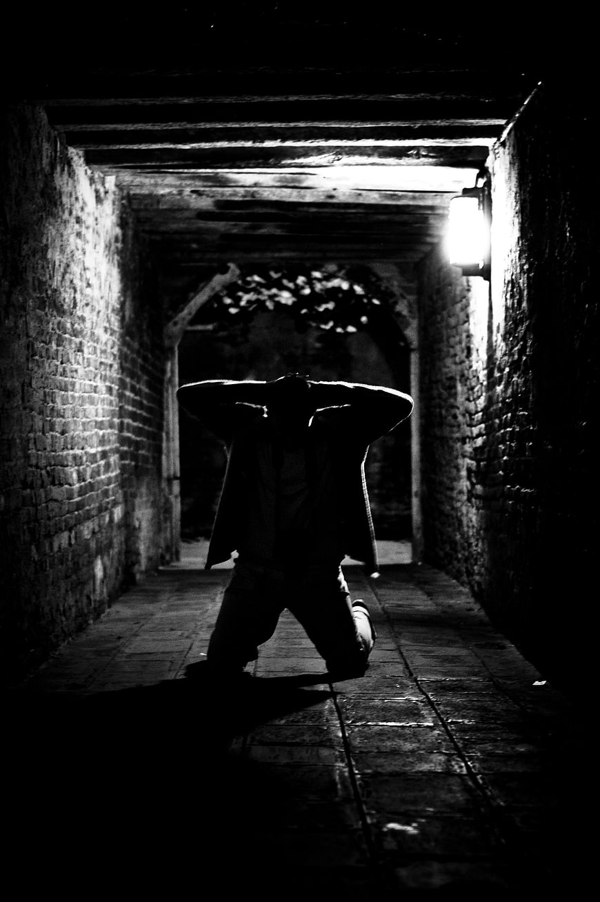 Dramatic Silhouette of Man Kneeling in Dark Brick Corridor