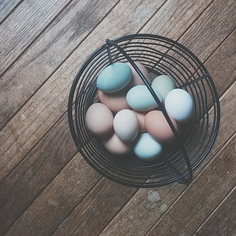 Top view of colorful eggs in a black wire basket on wood