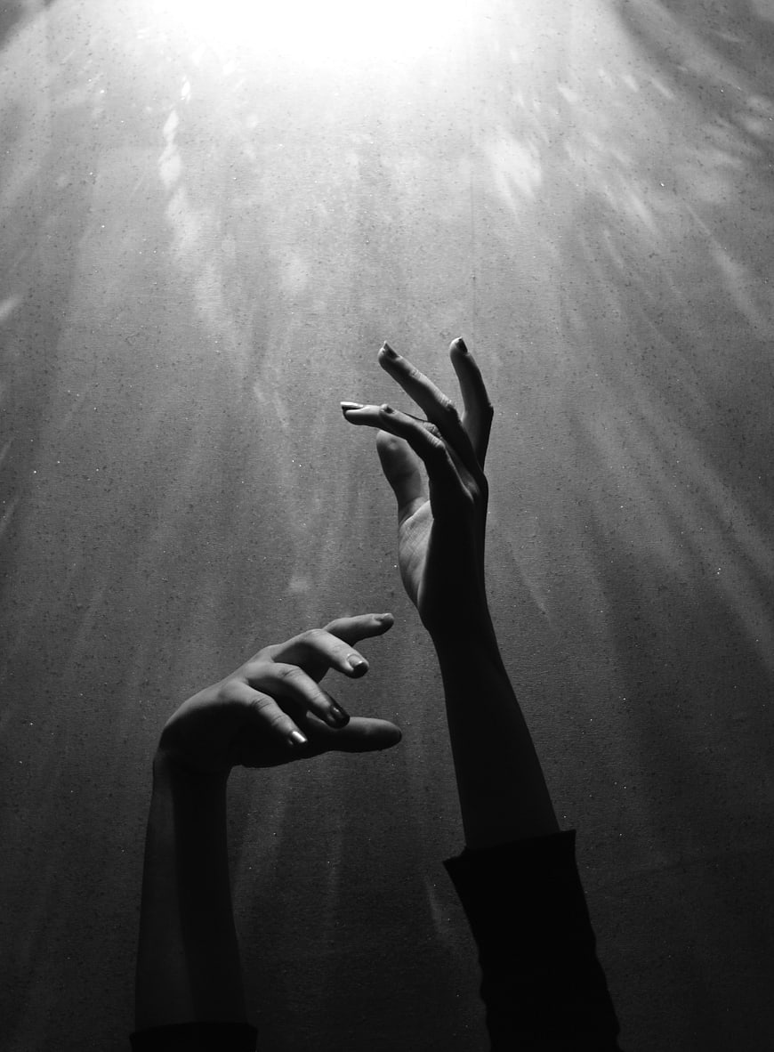 Silhouette of Hands Reaching for Light in Dark Atmosphere