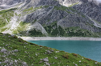 Alpine Lake Surrounded by Rocky Mountains and Green Slopes