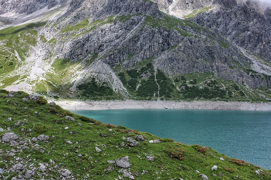 Alpine Lake Surrounded by Rocky Mountains and Green Slopes