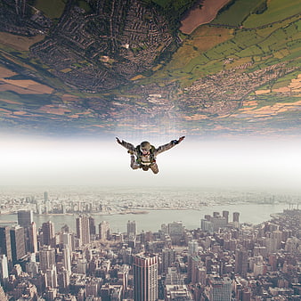 Skydiver in freefall between aerial city and inverted rural landscape