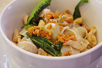 Close-up of Asian noodle bowl with chicken, greens, and fried garlic