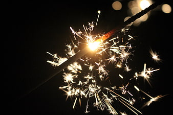 Close-up of a lit sparkler with bright sparks against a dark night background