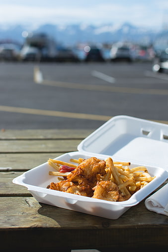 Fish and chips takeaway on wooden table with mountain view