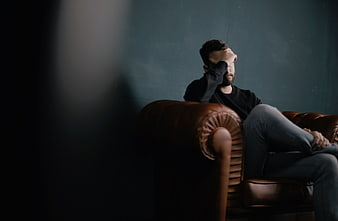 Man sitting on leather sofa with hand on forehead