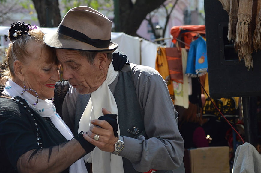 Senior couple embracing in traditional Argentine tango attire at outdoor market
