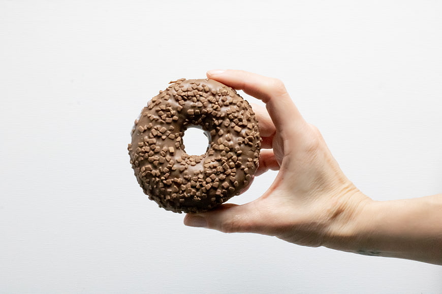Hand Holding Chocolate Sprinkled Donut on White Background