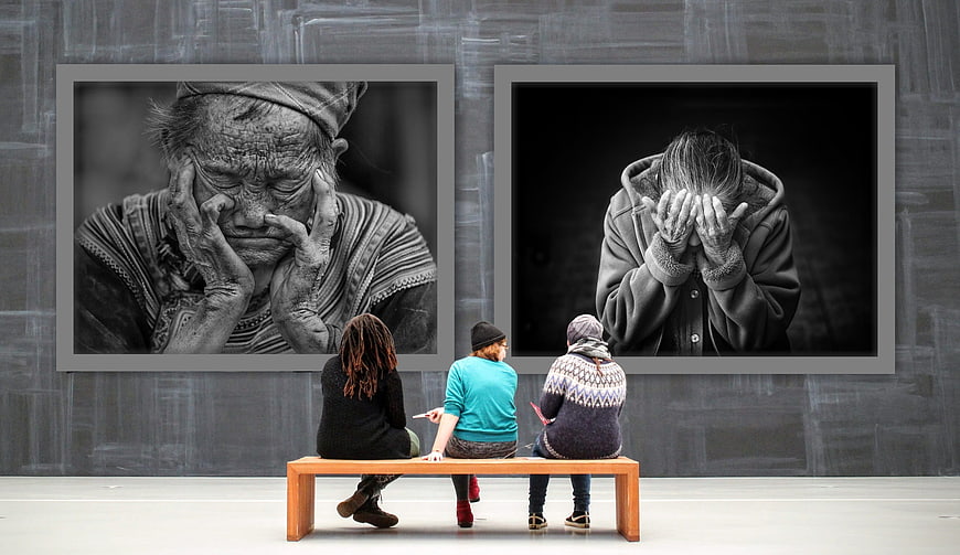 Three women viewing black and white portraits of despair in gallery